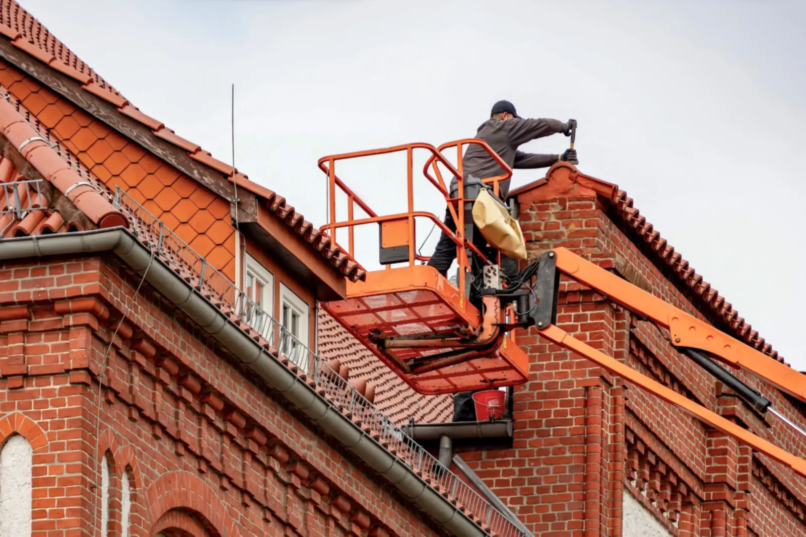 Werkman op een hoogwerker aan de dakrand van een bakstenen gebouw met een zinken dakgoot langs de dakvoet