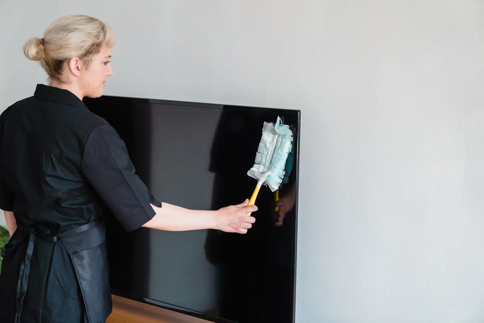 Schoonmaakster stoft een groot beeldscherm af tegen een lichte muur