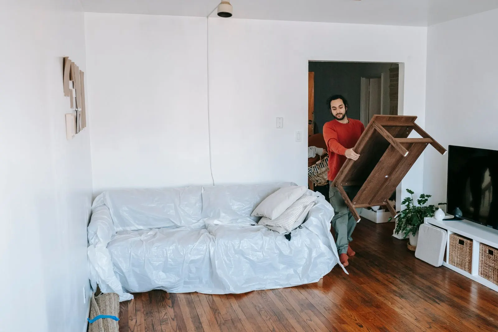 Man draagt een houten tafel door een lichte woonkamer met een zetel onder een beschermhoes