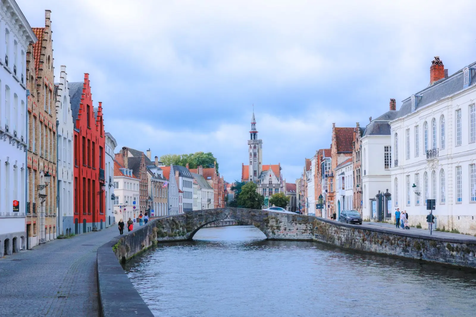 Gracht met stenen boogbrug en oude gevels in het historische centrum van Brugge, met een toren in de verte