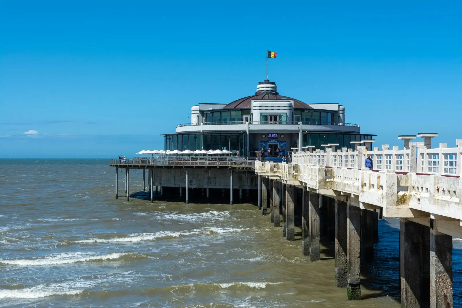 Pier van Blankenberge met paviljoen en Belgische vlag boven de golven van de Noordzee