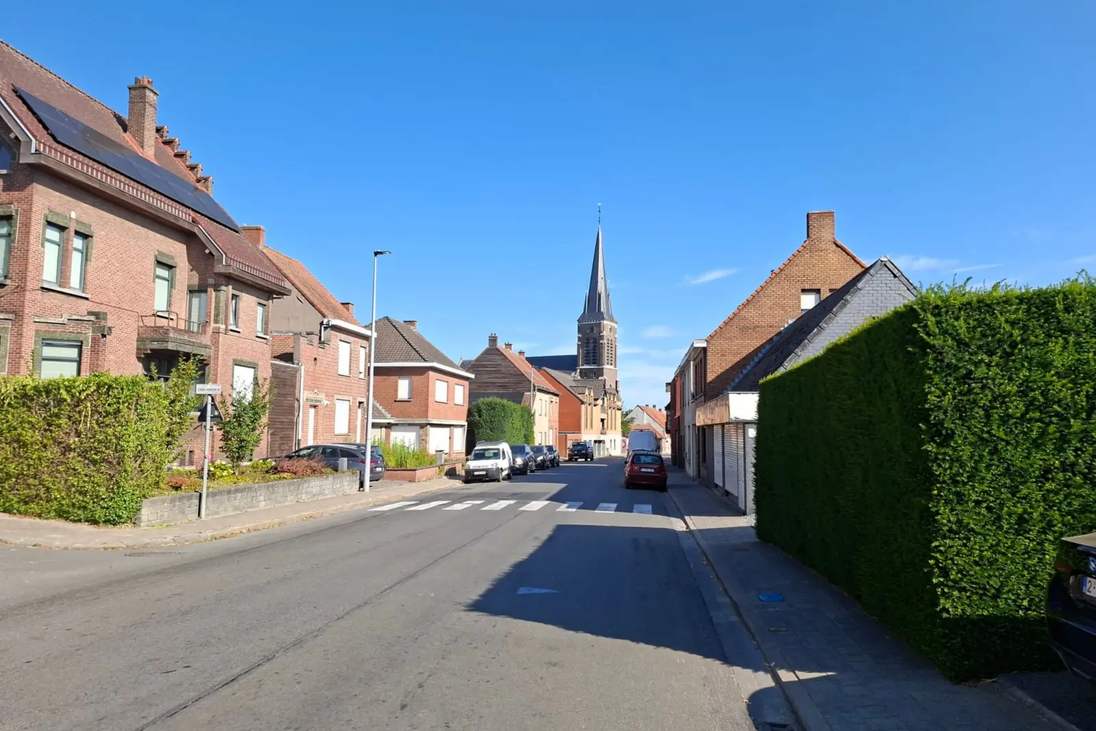 Straat met bakstenen woningen, een hoge haag en een kerktoren op de achtergrond in Ieper