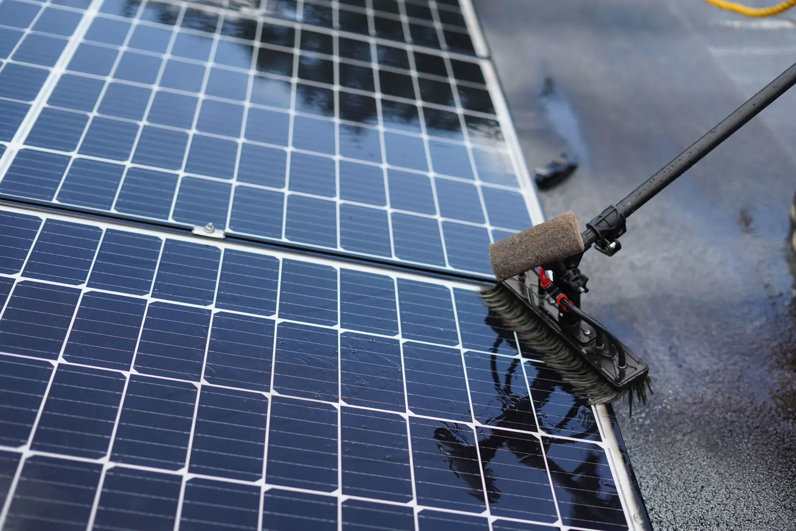 Close-up van een borstel op een telescoopsteel die natte zonnepanelen schoonborstelt